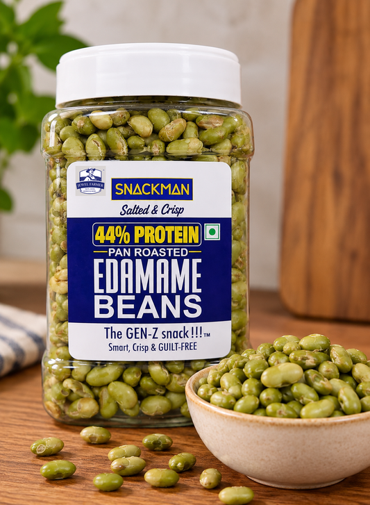 A jar of Snackman Pan Roasted Edamame Beans on a wooden table, with a small bowl of edamame and scattered beans in the foreground.