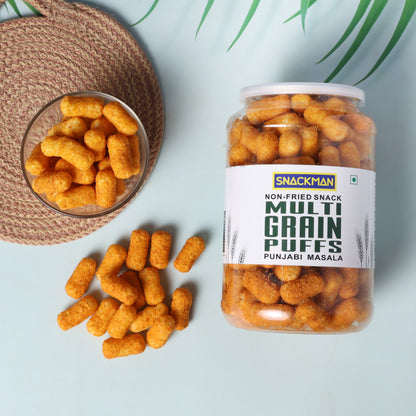 Jar of Snackman Multi Grain Puffs Punjabi Masala with a bowl and scattered puffs on a light blue background.
